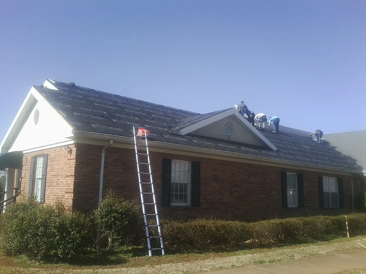 Crew tearing shingles off a brick ranch roof with a ladder set — Emergency Roof Repair work by our crew in Accord