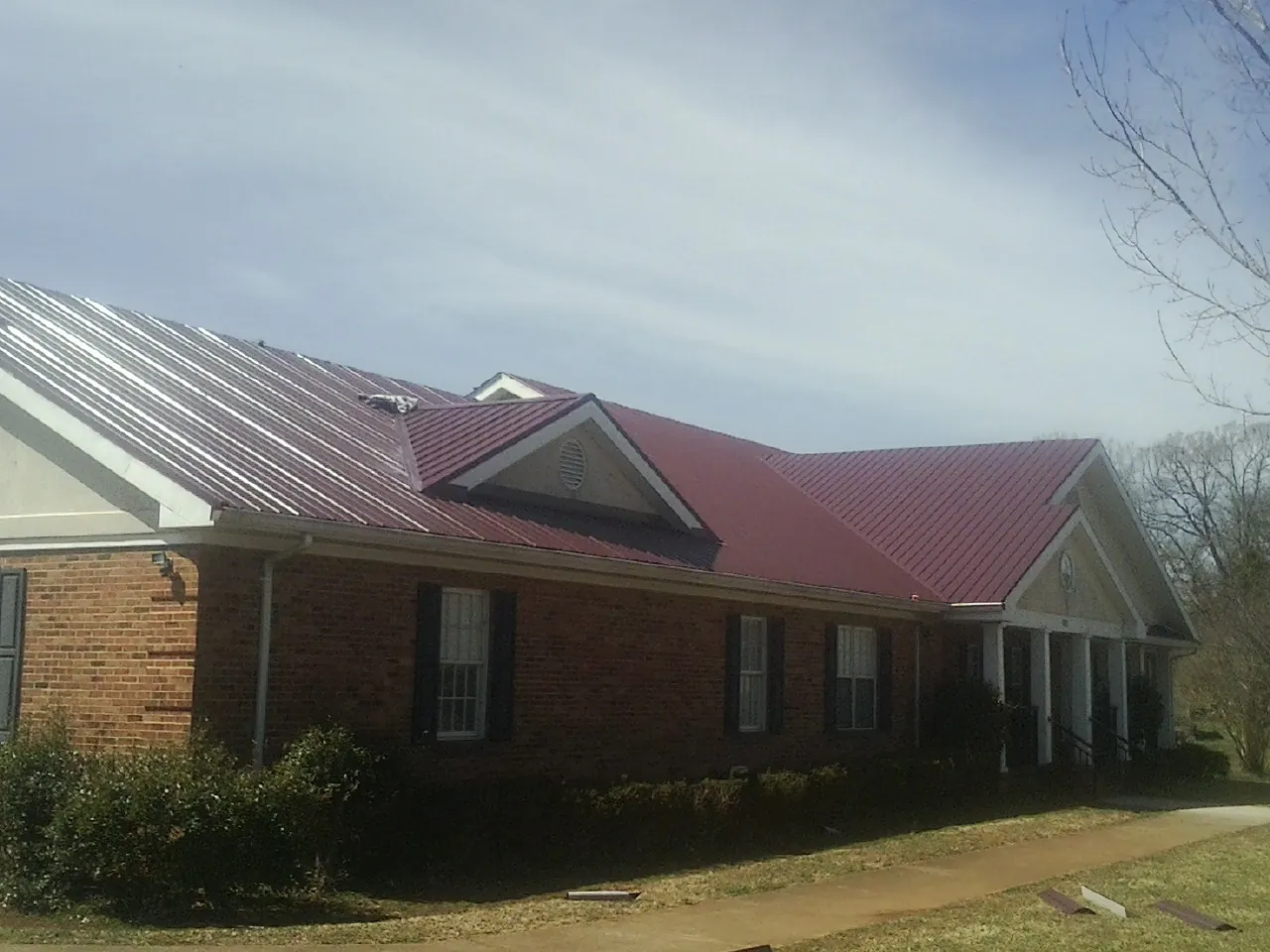 Red metal roof with gabled entries on a long brick building, from a Hail Damage Roof Repair job in Accord