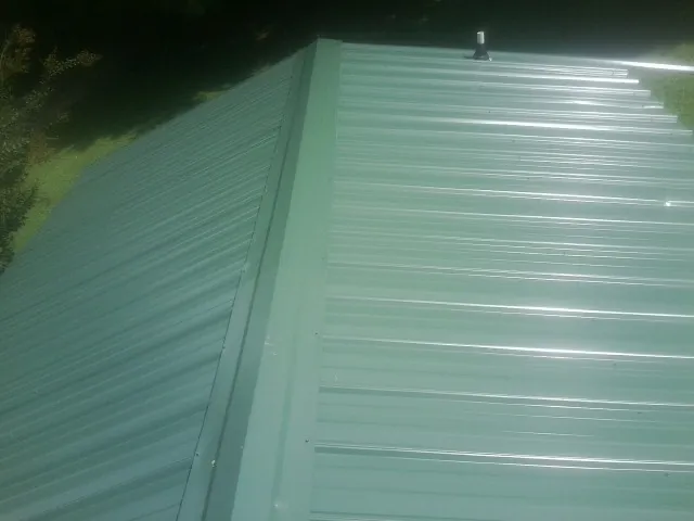 New green metal panels meeting at the ridge of a roof — Flat Roof Repair work by our crew in Accord