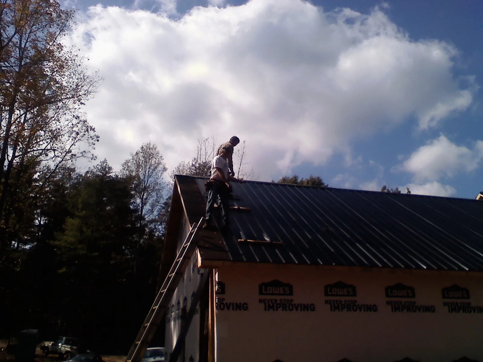 Roofer fastening dark metal panels high against a cloudy sky, from a Roof Inspection job in Accord