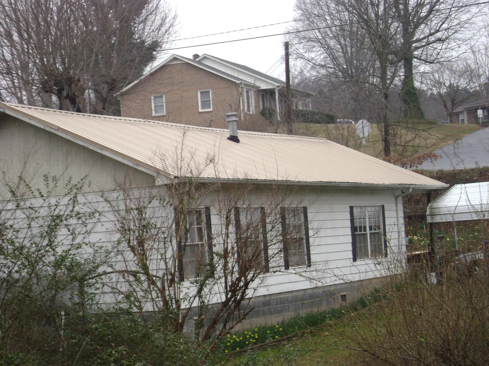 Tan metal roof on a white sided house set into a hillside — Commercial Roofing by Roofing Brothers in Accord